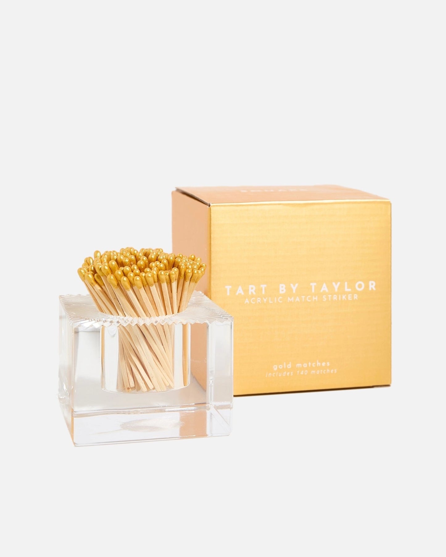 Tart by Taylor Acrylic Match Holder with Striker in a clear acrylic holder with gold match tips, shown next to its gold-colored packaging box on a light gray background.