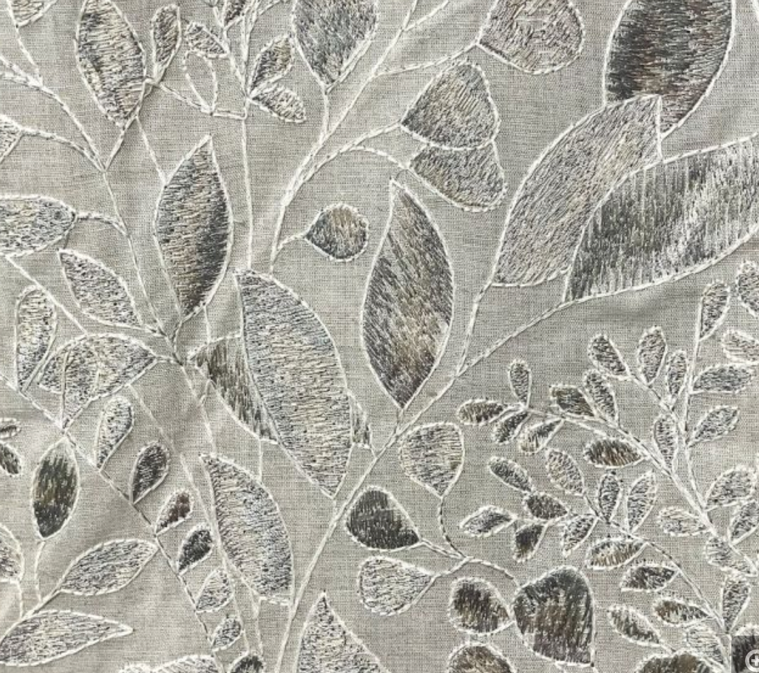 Close-up of a pillow embroidery design with floral motifs in silver color on a fabric background.