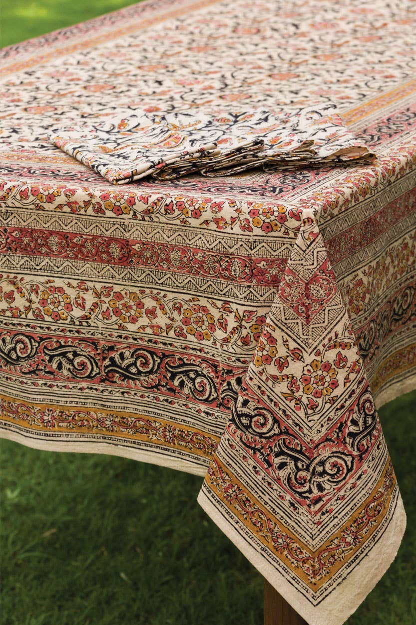 Rose-patterned tablecloth draped on table, cream base with red, green, black accents