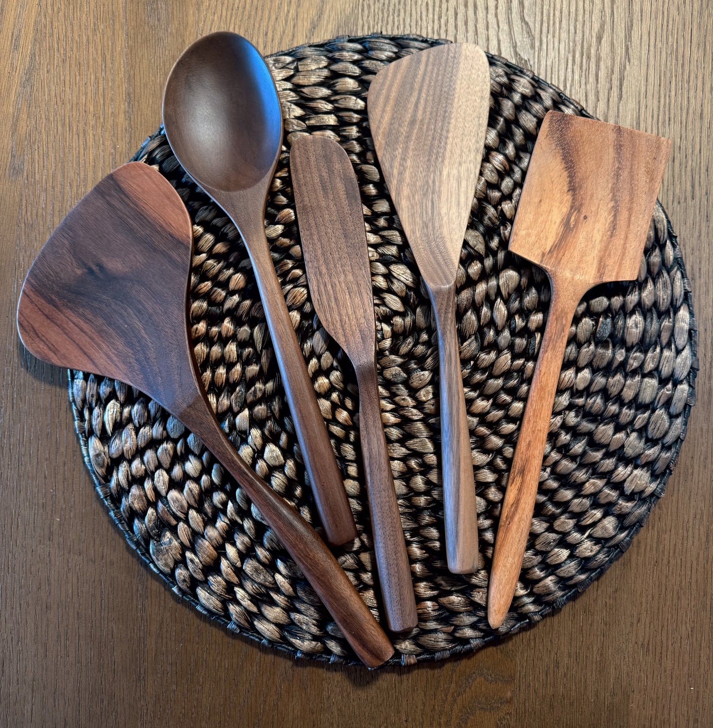 Carved wooden utensil set with spoon and spatulas, on round woven tray