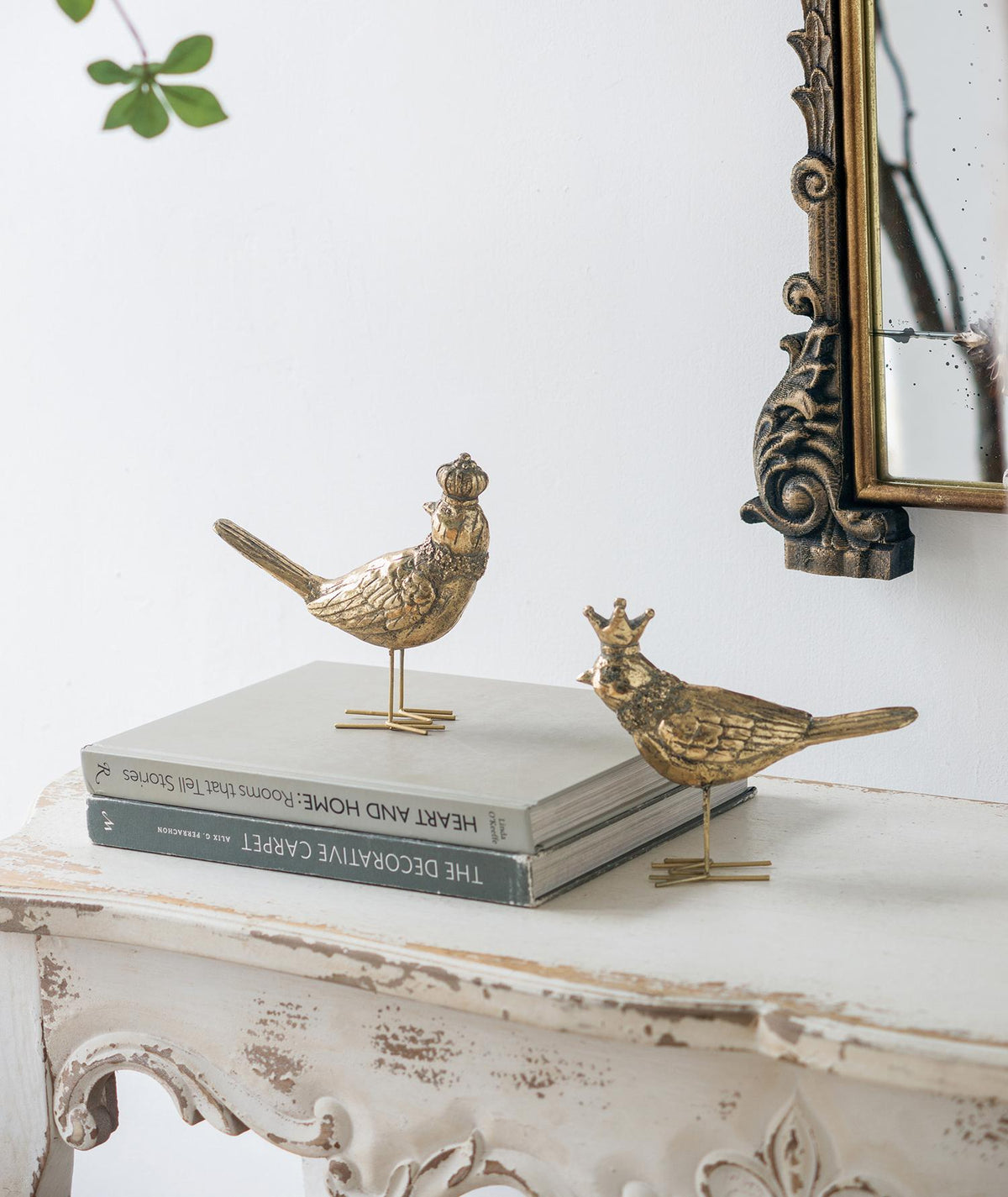Two gold bird figurines on books with a decorative mirror in the background.