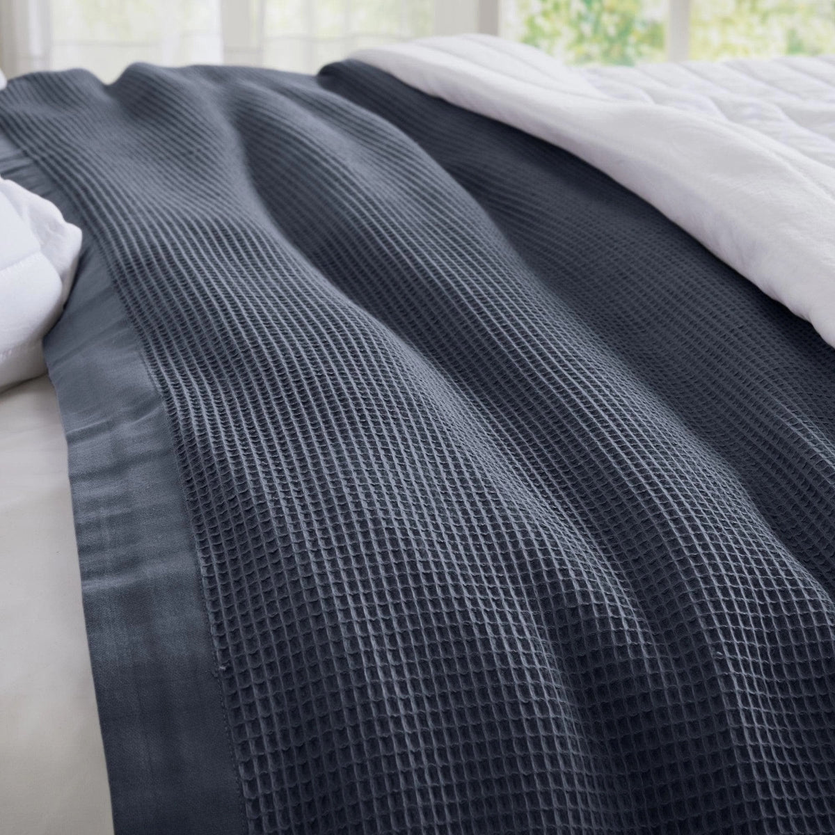 Dark gray textured blanket on a bed with white bedding