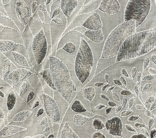 Close-up of a pillow embroidery design with floral motifs in silver color on a fabric background.