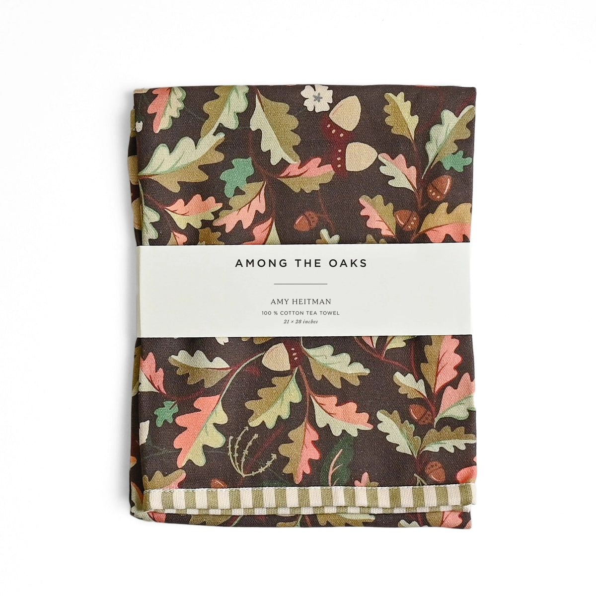 A folded fabric item with an autumn leaf pattern on a dark brown background, wrapped with a white paper band labeled 'AMONG THE OAKS' and 'AMY HILTMAN'.