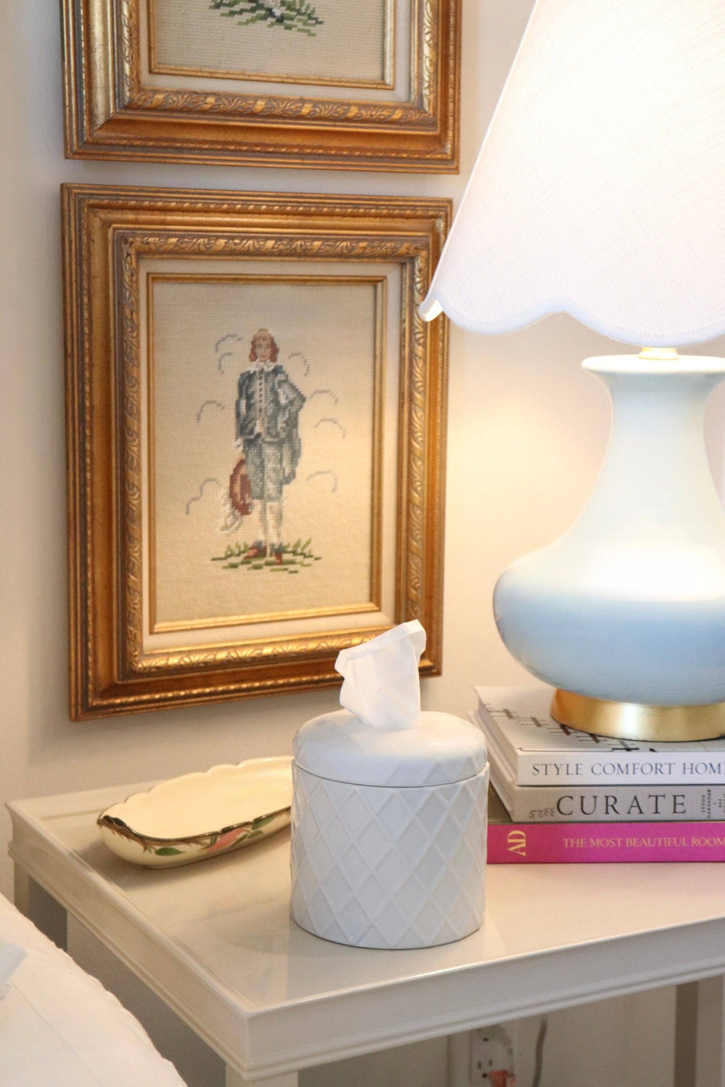 Decorative table with framed artwork, lamp, tissue box, and books on a light-colored surface.