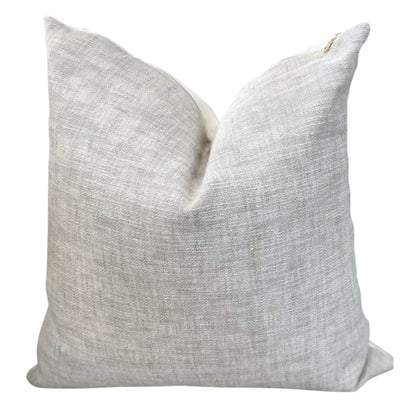 A beige linen throw pillow with an exposed brass zipper on the front.