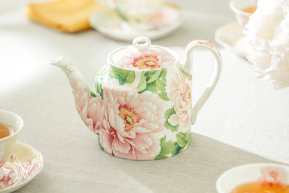 Floral teapot on a table with tea cups and a plate
