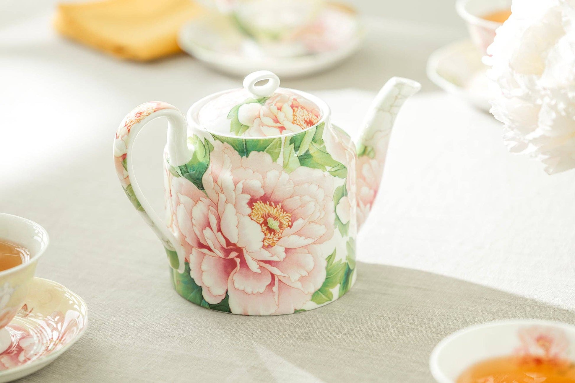 Teapot with floral design on a table with tea cups and saucers.