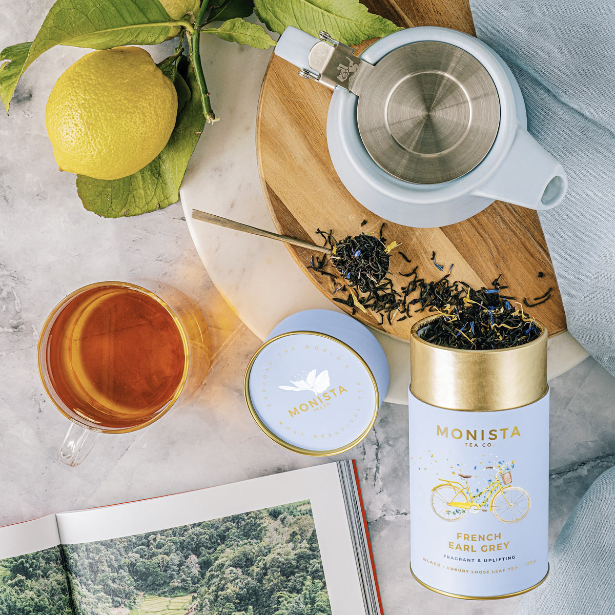 Tea set with Monista tea canisters, a teapot, and a cup on a marble surface.