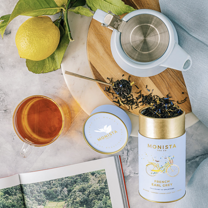 Tea set with Monista tea canisters, a teapot, and a cup on a marble surface.