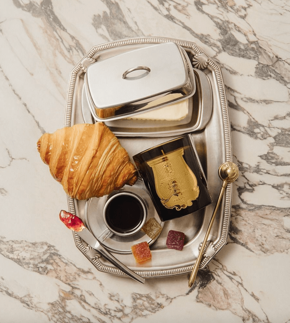 Trudon Gabriel Candle styled on a marble surface alongside a silver tray, croissant, and coffee for a luxurious French morning vignette.