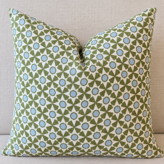 A square throw pillow with a geometric pattern of green triangles and light blue circles on an off-white background, set against a neutral beige textured backdrop.