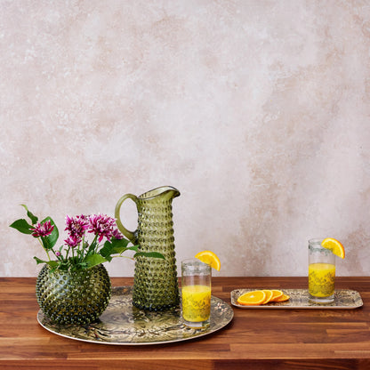 Green textured pitcher and glasses with orange juice on a wooden table against a beige wall.