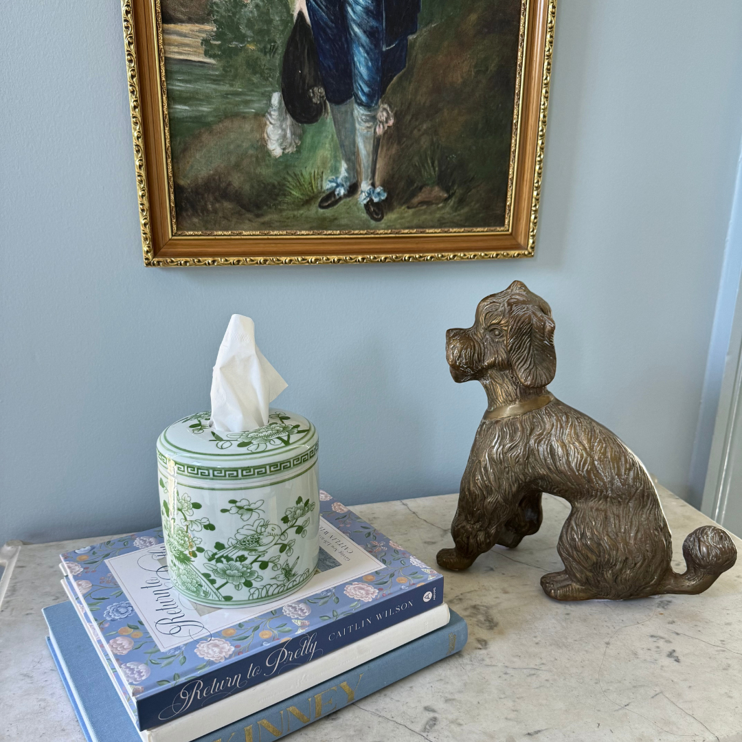 Decorative items including a tissue box, books, and a bronze dog statue on a surface with a painting in the background.
