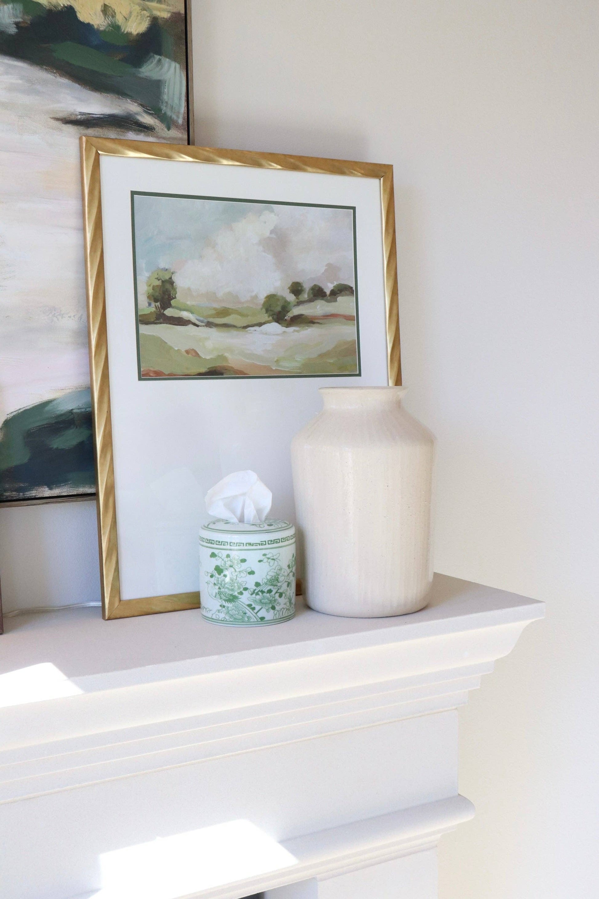 Framed landscape painting on a shelf with a vase and tissue box.
