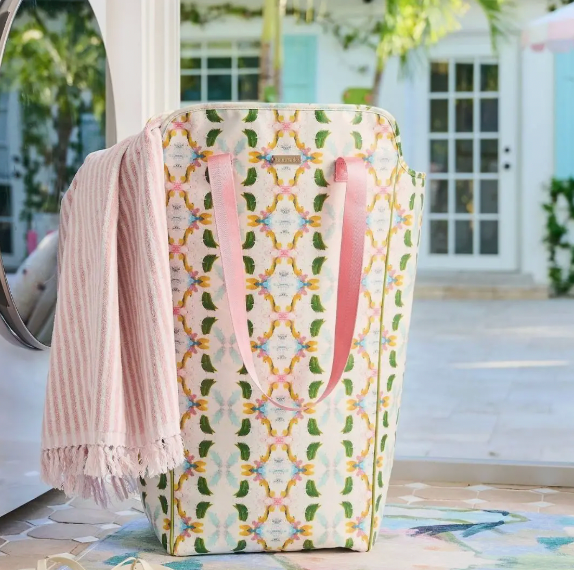 Patterned tote bag with pink handles and a blanket draped over it, set against a blurred outdoor background.