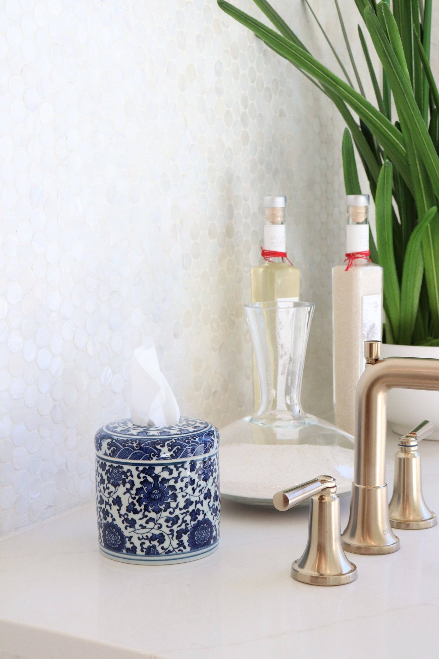 Bathroom counter with a blue and white ceramic jar, glass bottles, and metallic faucet.