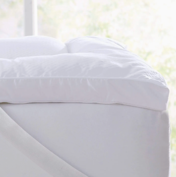White fitted sheet on a bed with a blurred window background