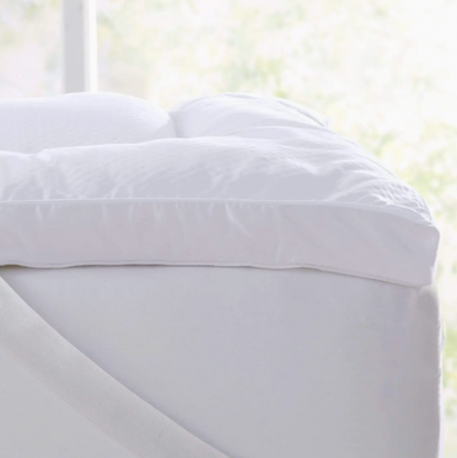 White fitted sheet on a bed with a blurred window background