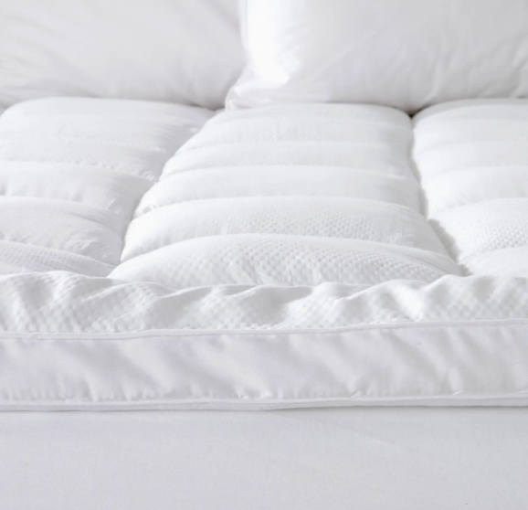 Close-up of a white quilted mattress topper on a bed.