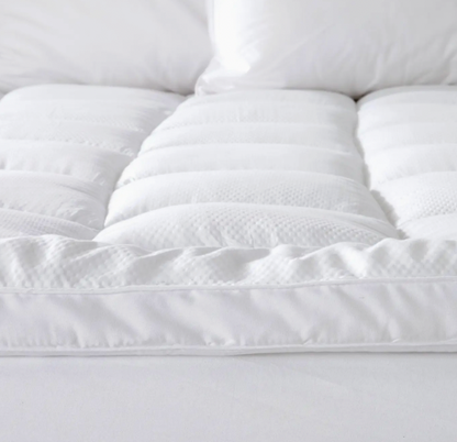 Close-up of a white quilted mattress topper on a bed.