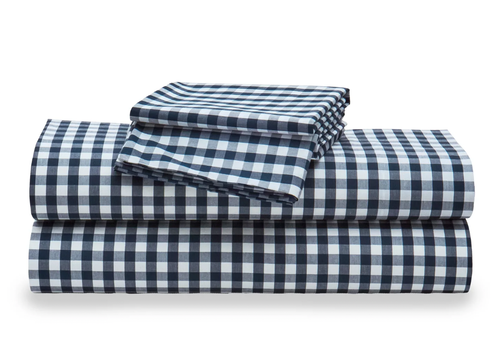 A stack of white percale sheet sets with blue stripes on the edges, neatly folded.