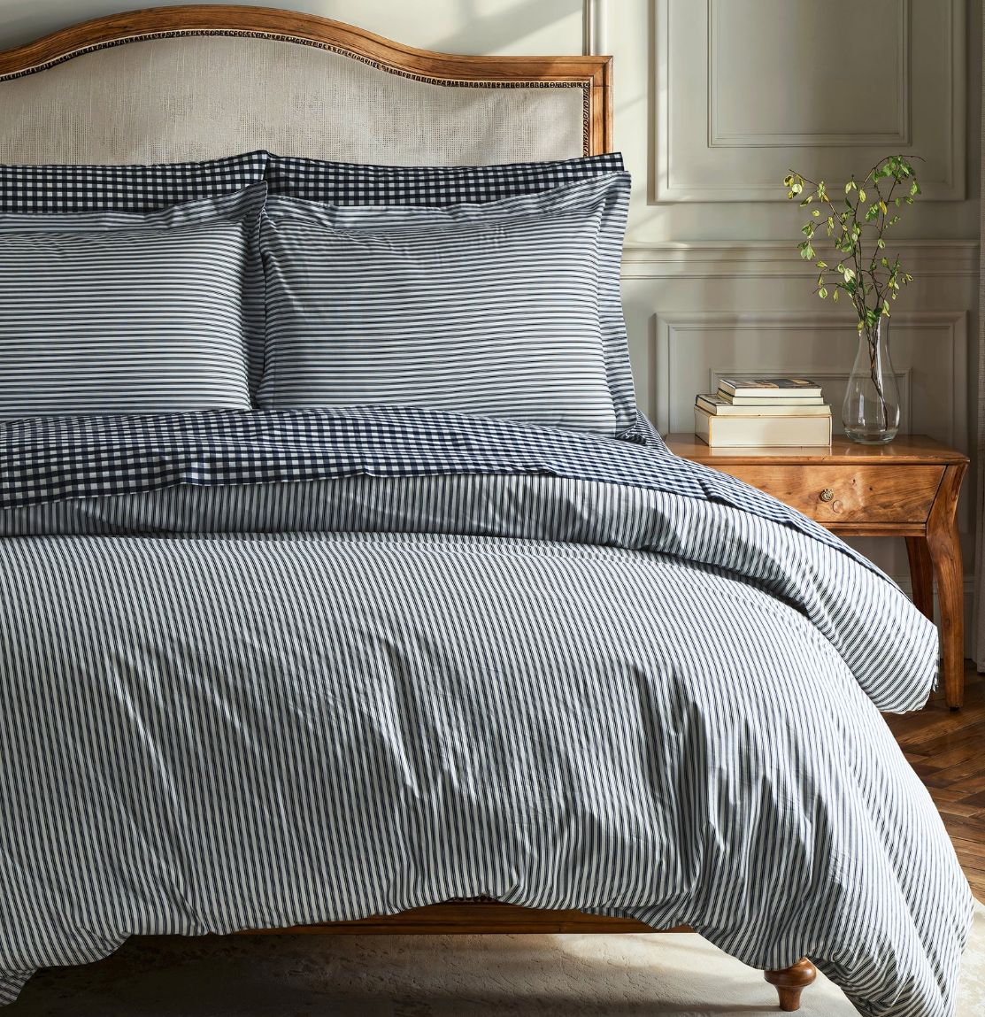 A stack of white percale sheet sets with blue stripes on the edges, neatly folded.