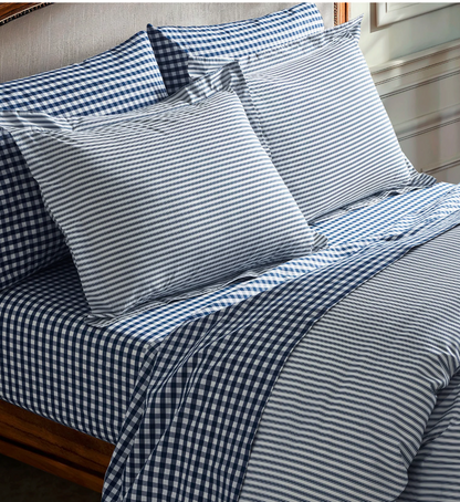 A stack of white percale sheet sets with blue stripes on the edges, neatly folded.