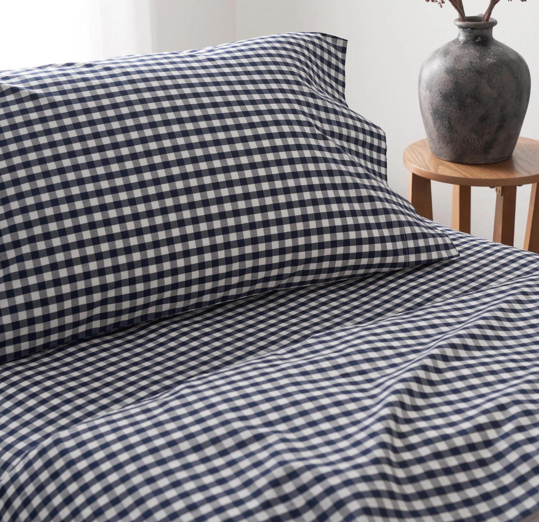 A stack of white percale sheet sets with blue stripes on the edges, neatly folded.