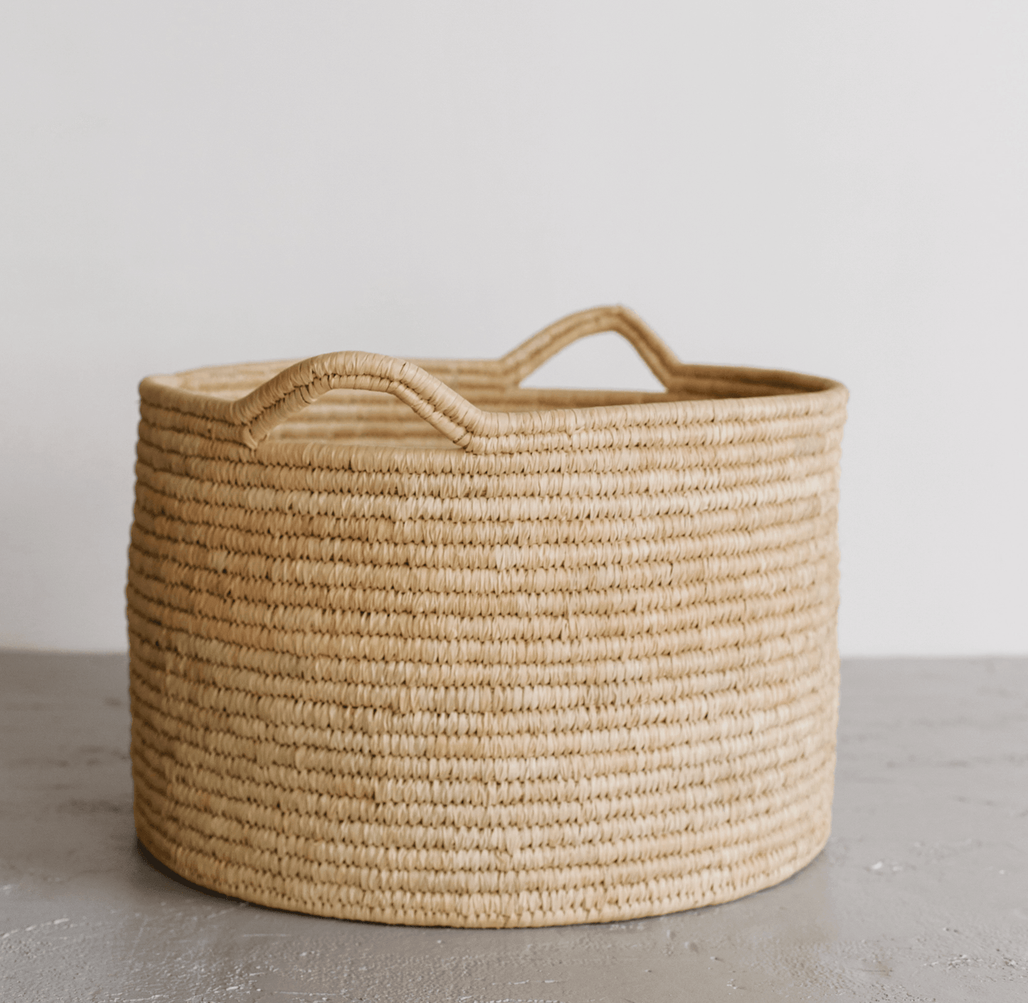 Woven Palm Leaf laundry basket with handles on a neutral background