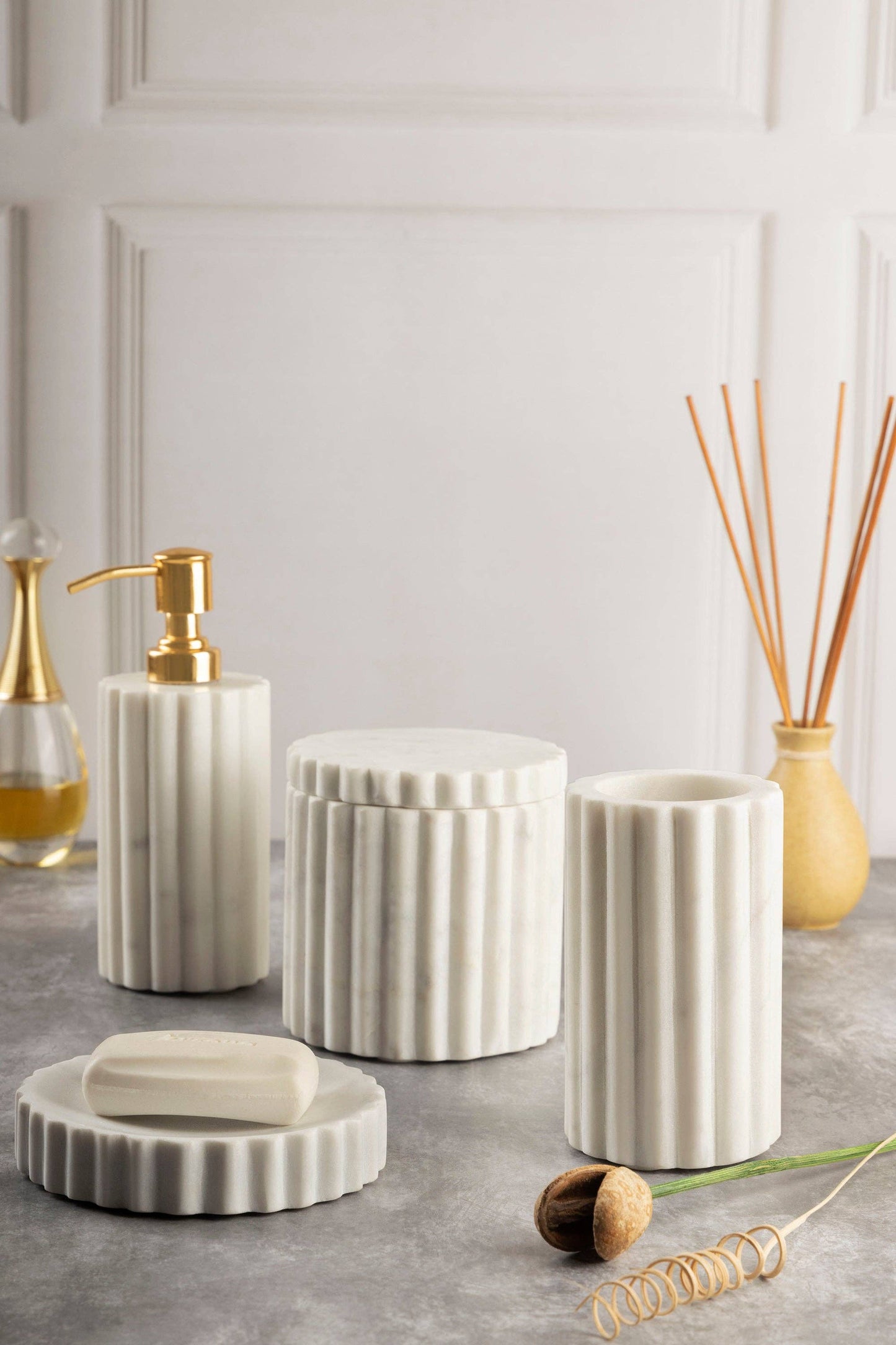 Set of white ceramic bathroom containers with gold accents on a gray surface.
