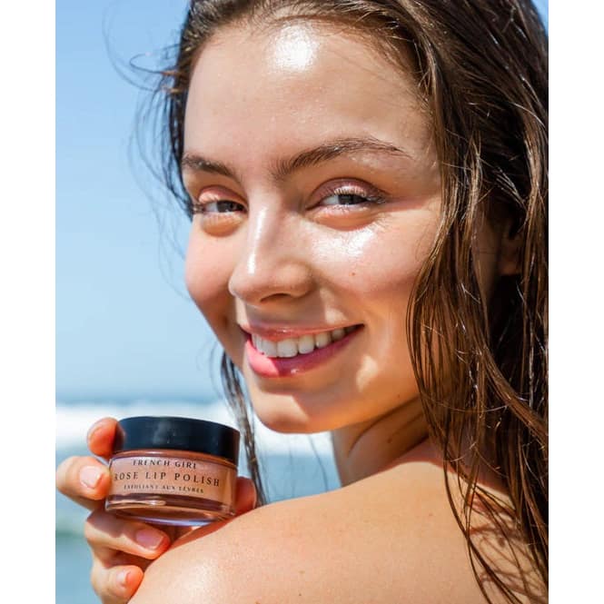 Woman holding a jar of 'French Girl' lip polish with a beach background