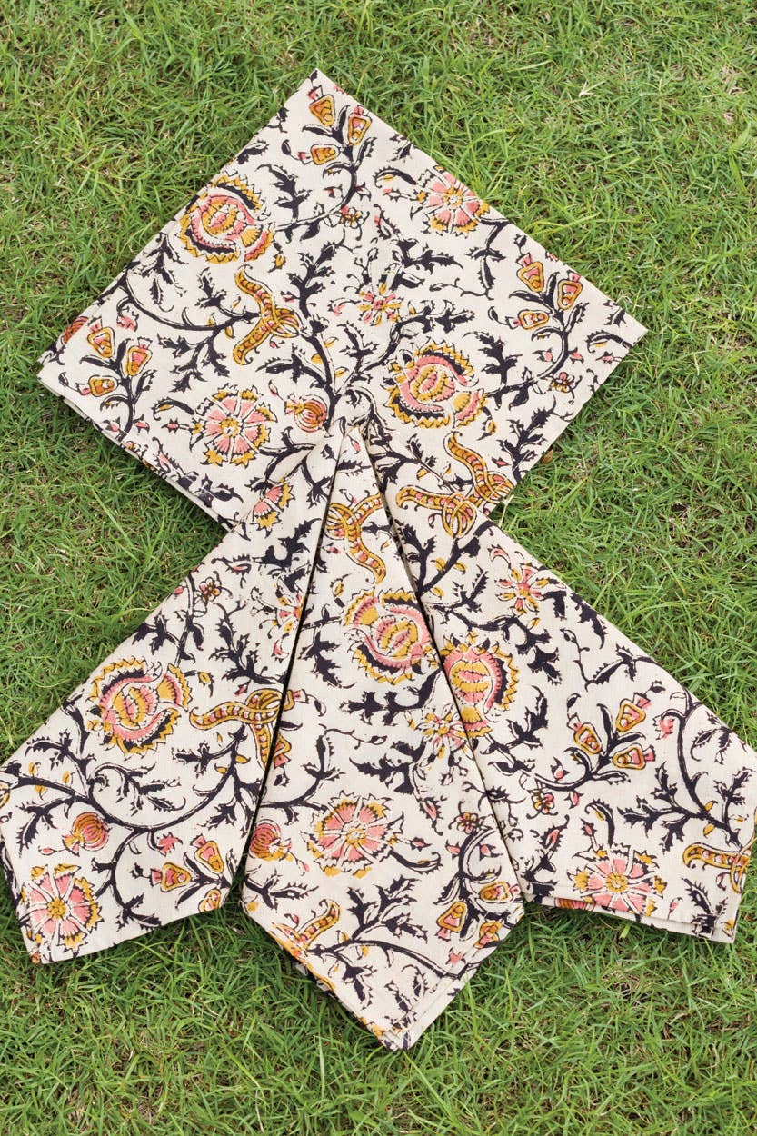 Light cream dinner napkin with ornate rose-and-paisley print, folded into star shape
