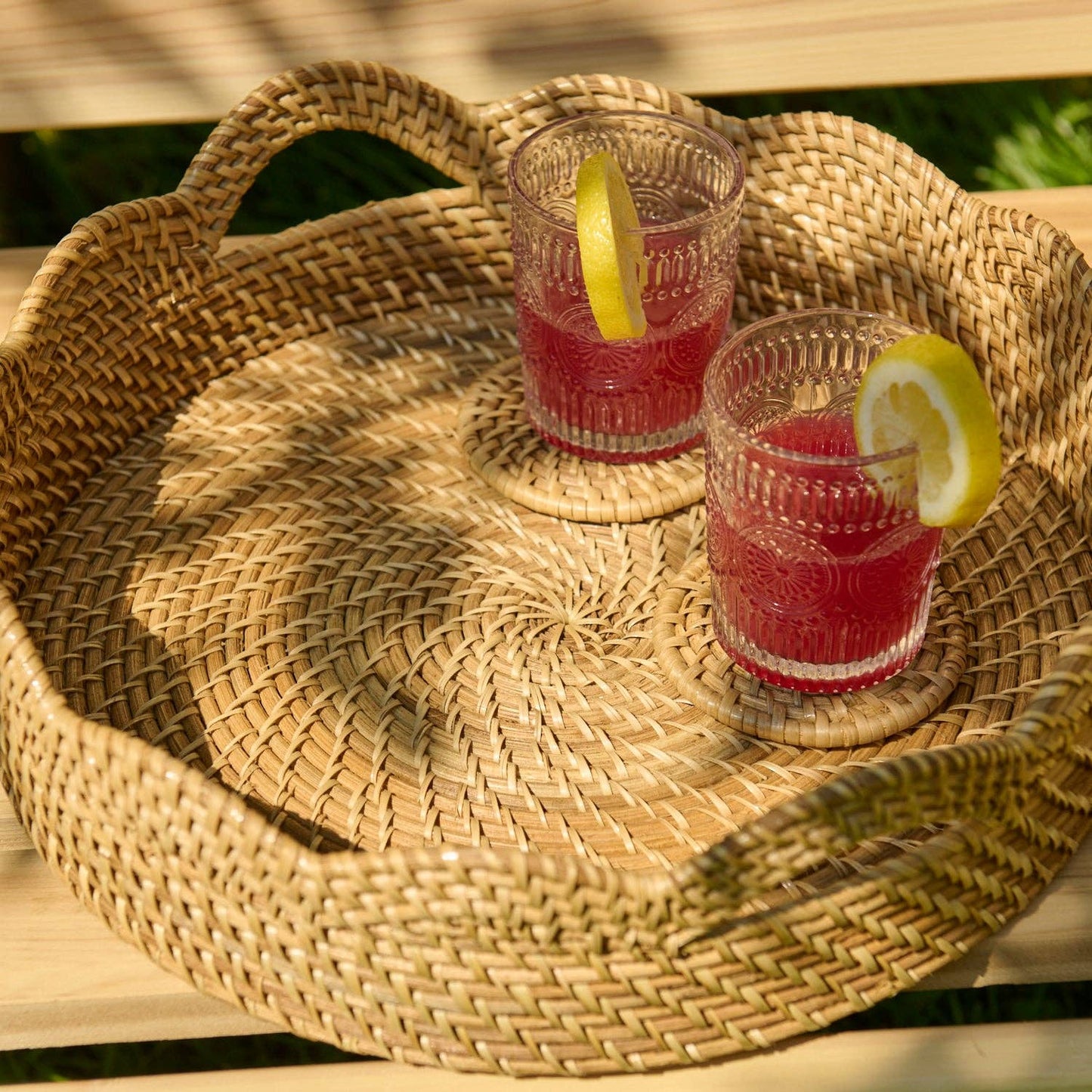 Two glasses of red lemonade on a woven tray outdoors.