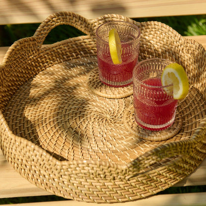 Two glasses of red lemonade on a woven tray outdoors.