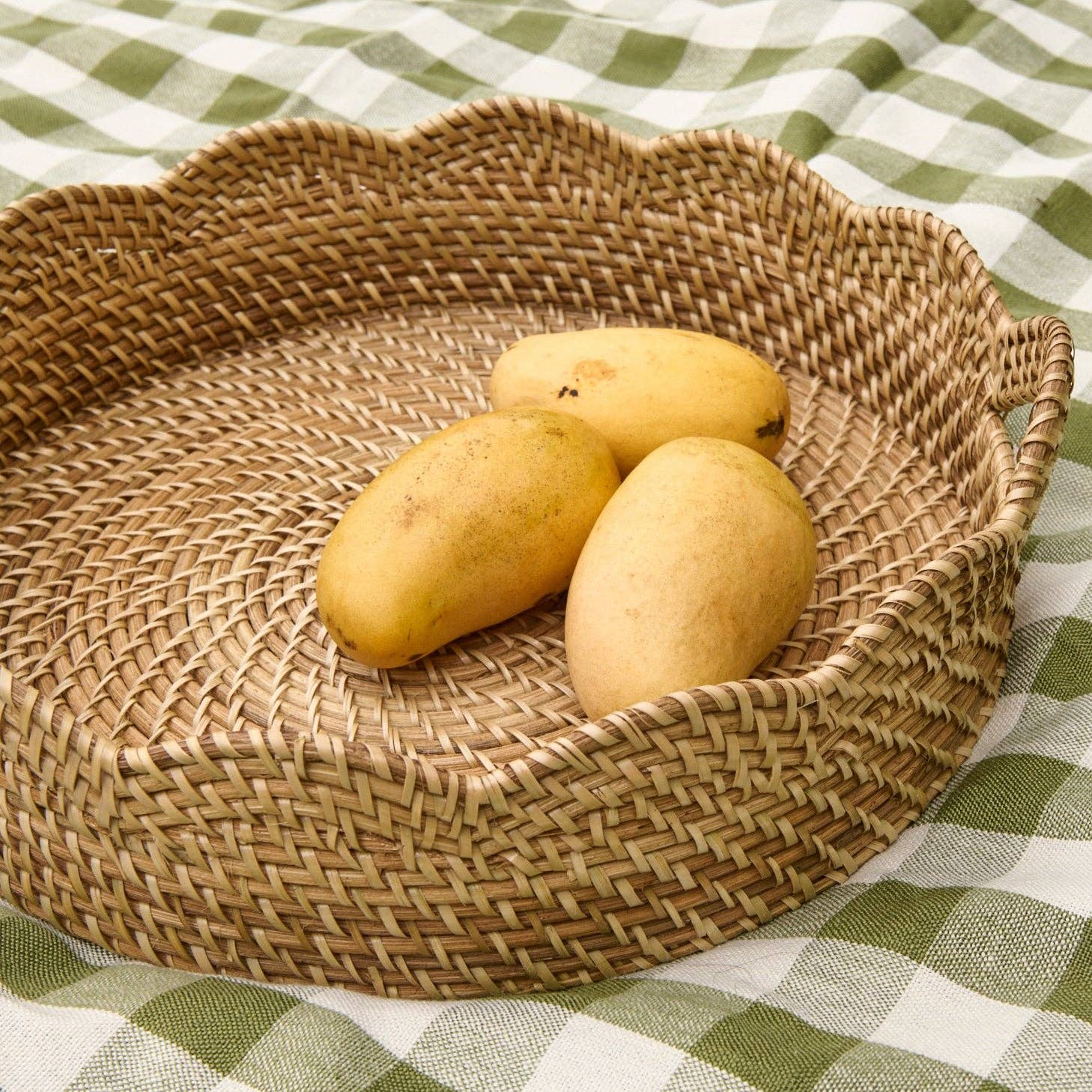 Three mangoes in a woven basket on a green and white checkered tablecloth