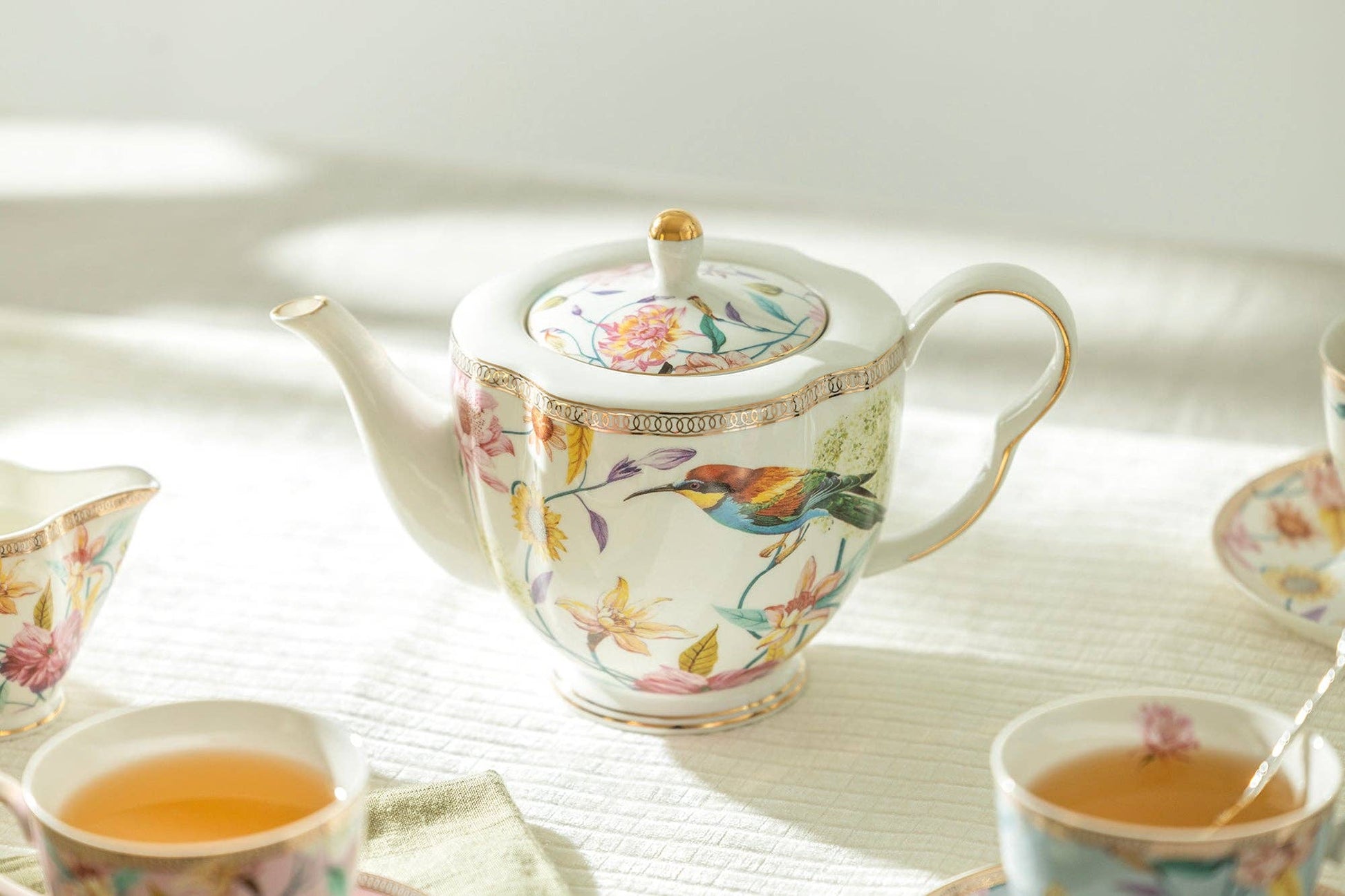 Decorative teapot and cups with floral patterns on a light surface