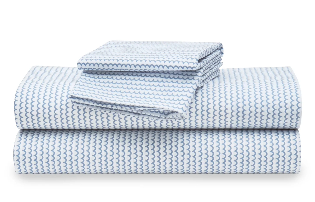 A stack of white percale sheet sets with blue stripes on the edges, neatly folded.