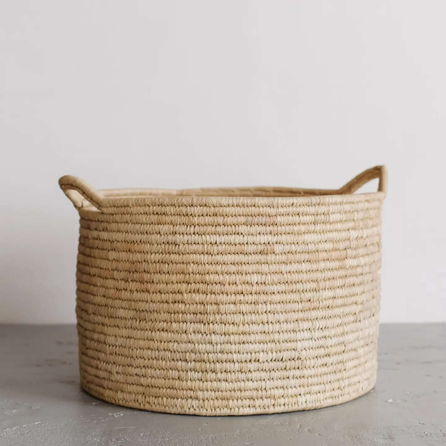 Woven Palm Leaf laundry basket with handles on a plain background