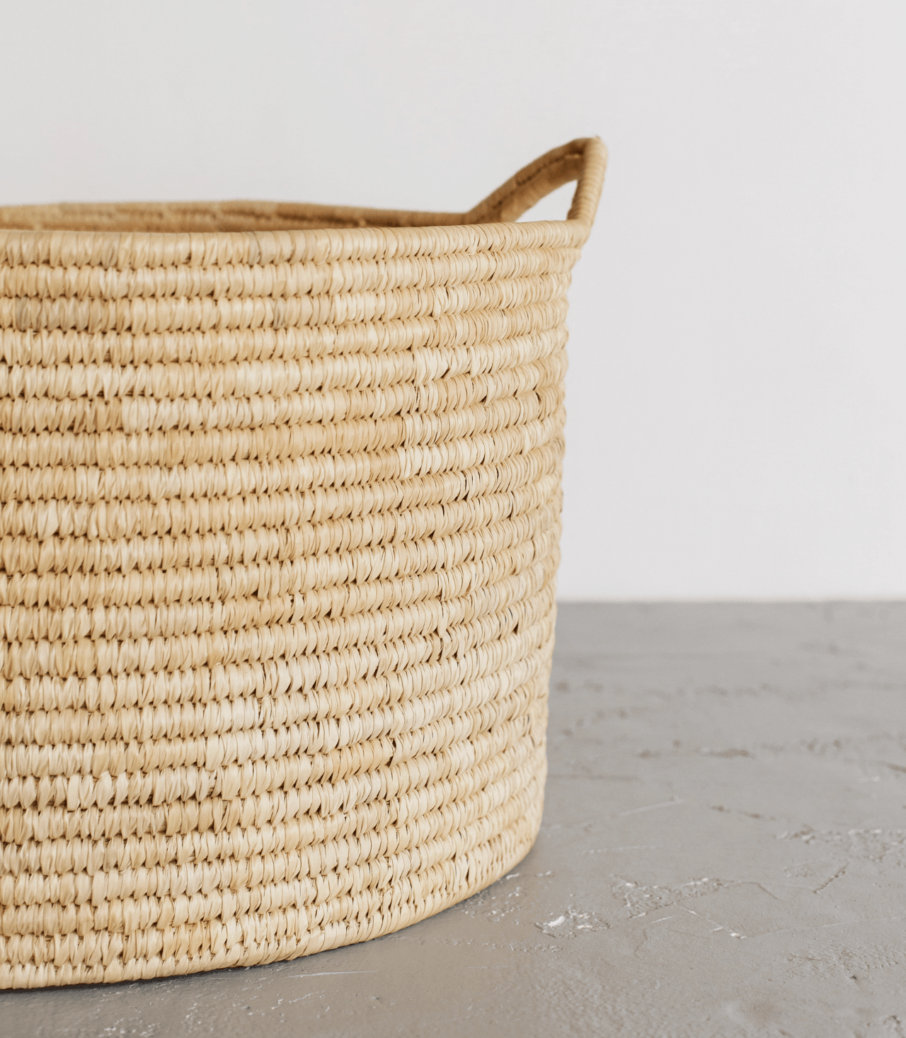 Woven Palm Leaf laundry basket on a gray surface with a white background