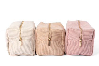 Three corduroy cosmetic bags in light, nude, and rose pink with gold zippers