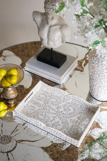 Decorative table setting with a marble bust, books, lemons, and a textured tray.