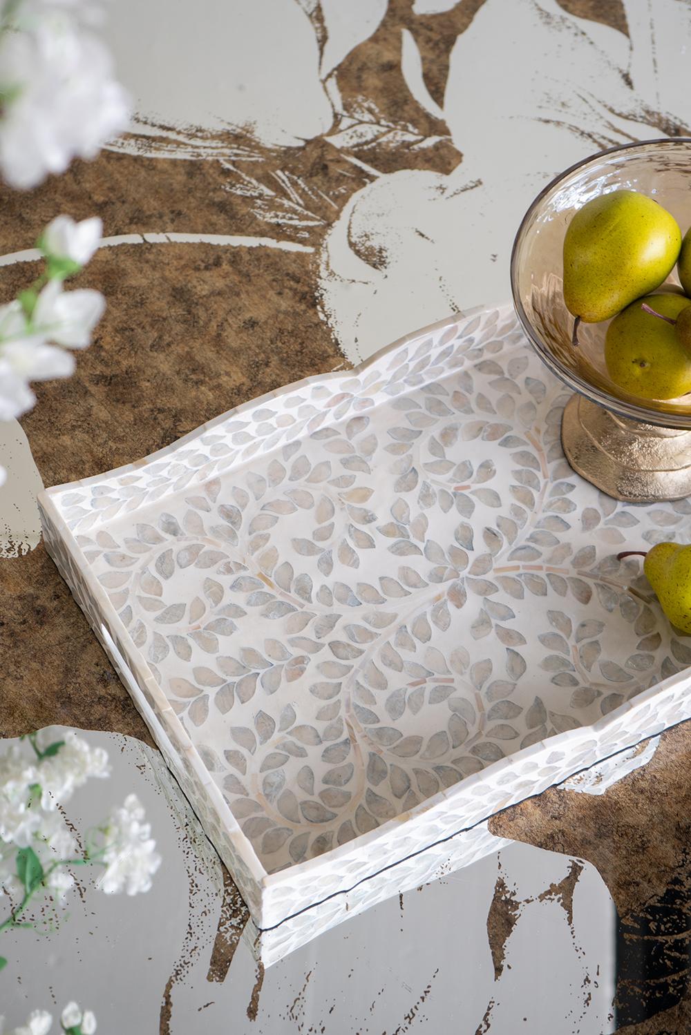 Decorative tray with leaf pattern on a rustic surface with pears and flowers.