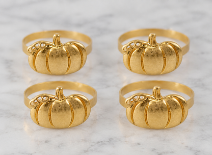 Four gold pumpkin-shaped rings arranged in a 2x2 grid on a white marble surface.
